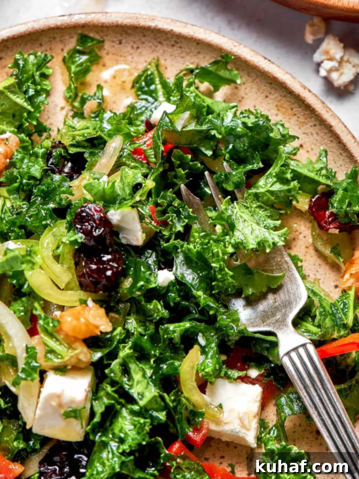 A generous portion of vibrant chopped kale salad, artfully arranged on a white plate, with extra cranberries and walnuts visible on top for garnish.