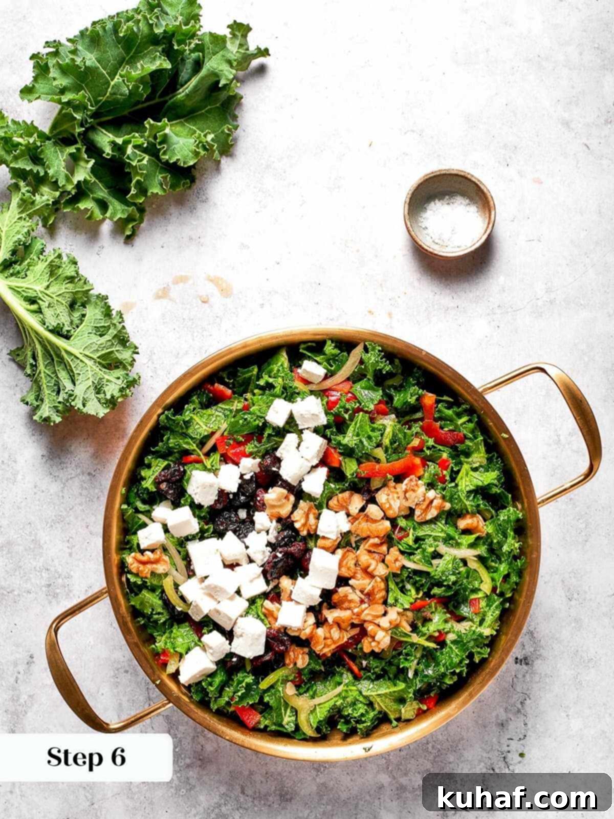 Crumbled feta cheese being sprinkled generously into the kale salad during the final preparation stages, adding a savory tang.