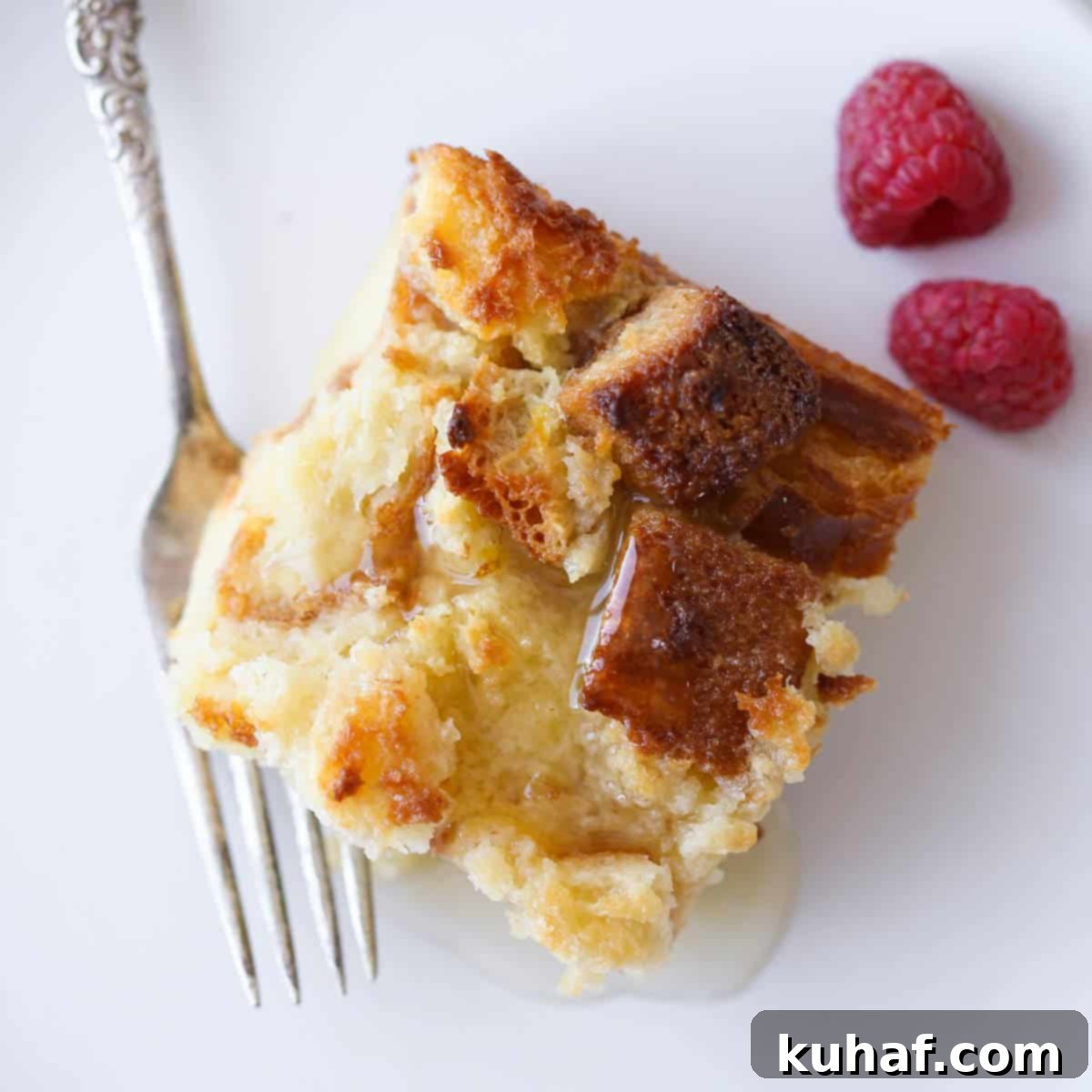 A slice of Lemon Raspberry Bread Pudding on a white plate, garnished with fresh raspberries