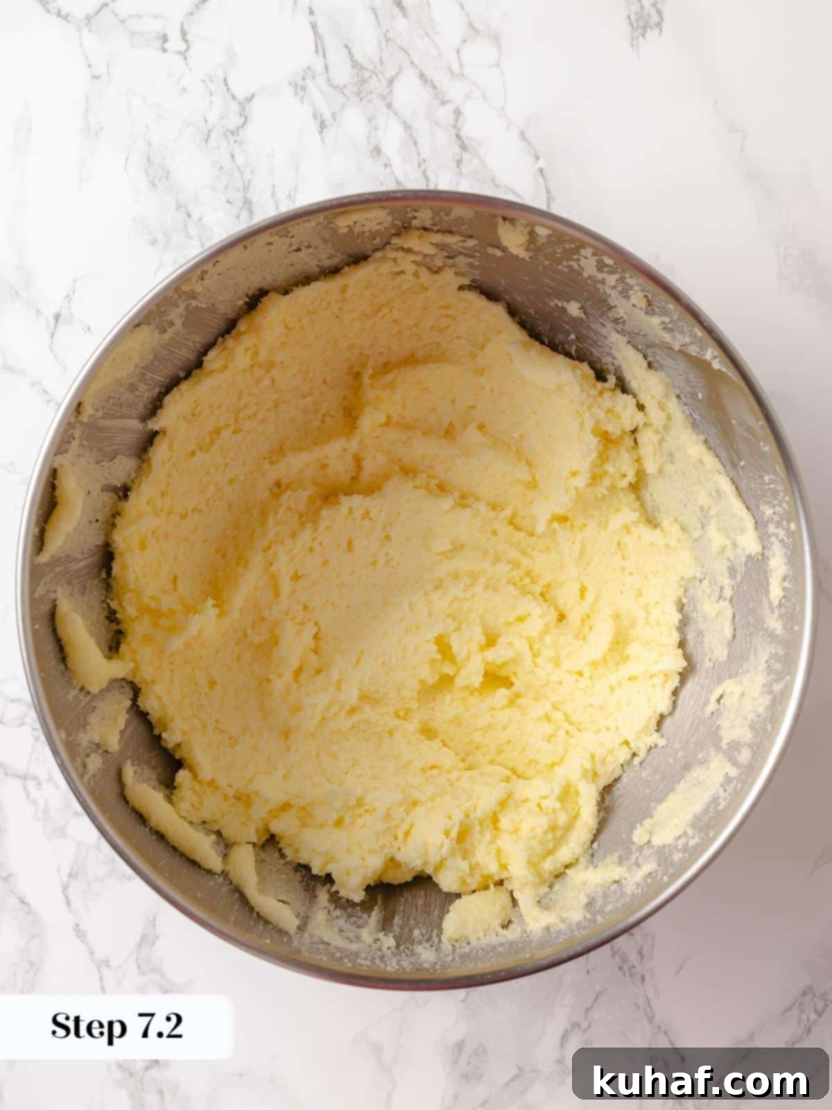 Butter and sugar after being beaten into a thick, pale, and fluffy paste in a mixing bowl, indicating proper creaming.