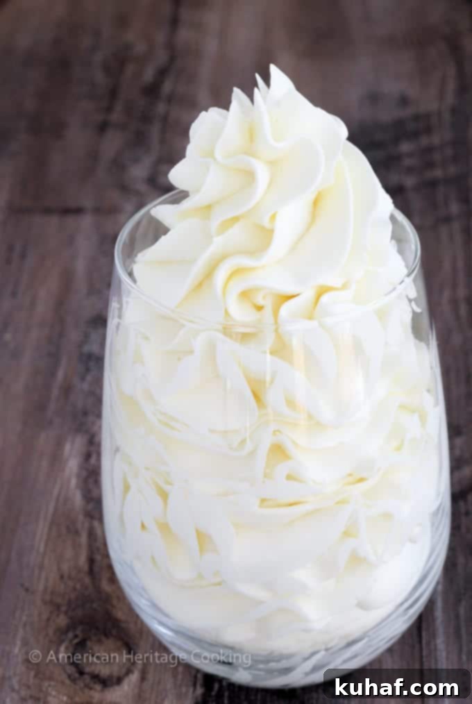 Italian meringue buttercream in a clear glass against a wooden backdrop, showcasing its smooth texture.