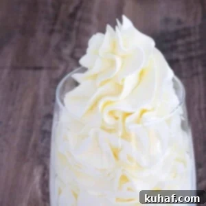 Italian meringue buttercream cleanly piped into a clear glass with a little sticking out of the top, looking fluffy and ready to use.
