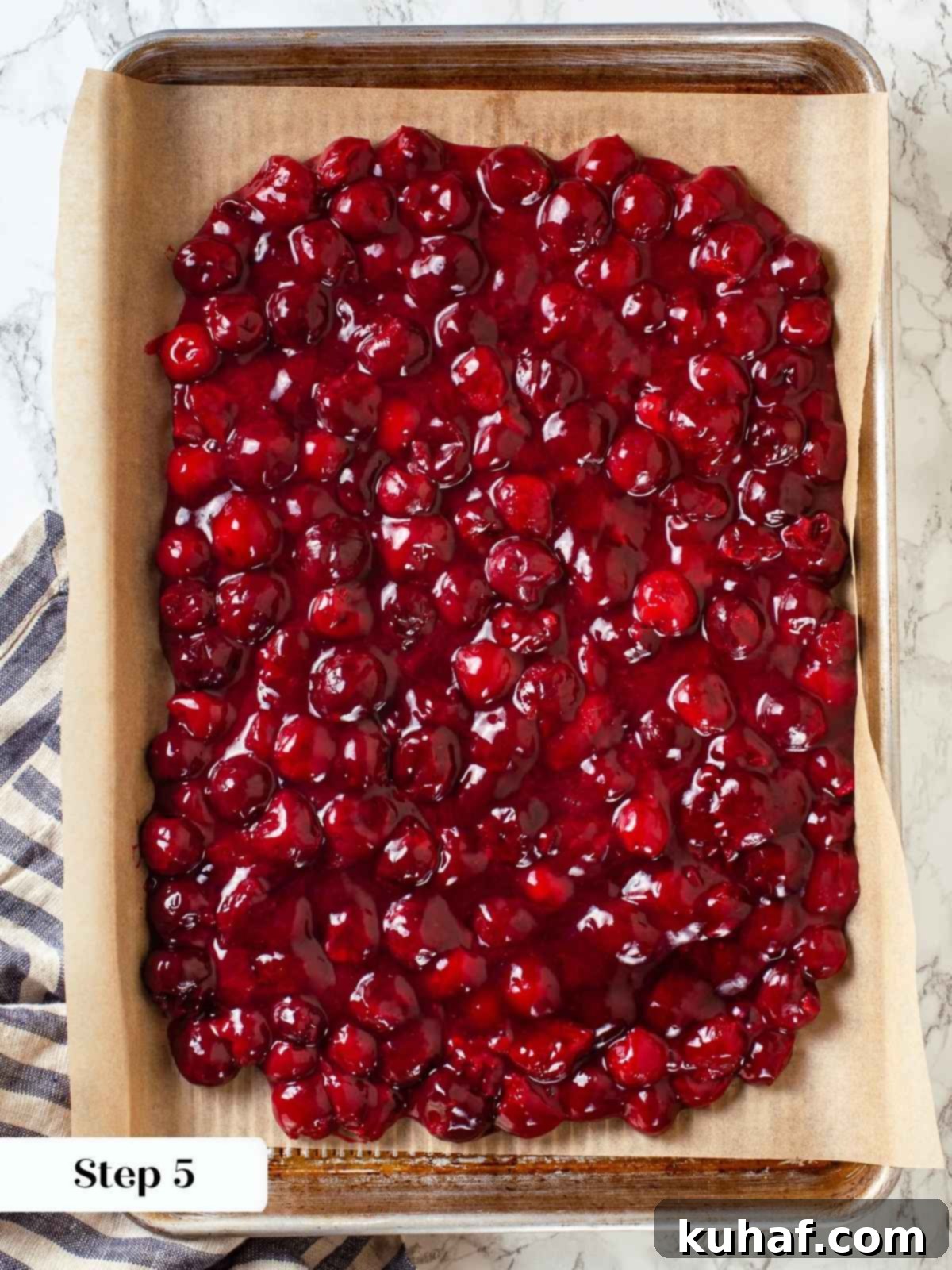 Finished cherry pie filling cooling on parchment-lined baking sheet, deep red and glossy throughout.