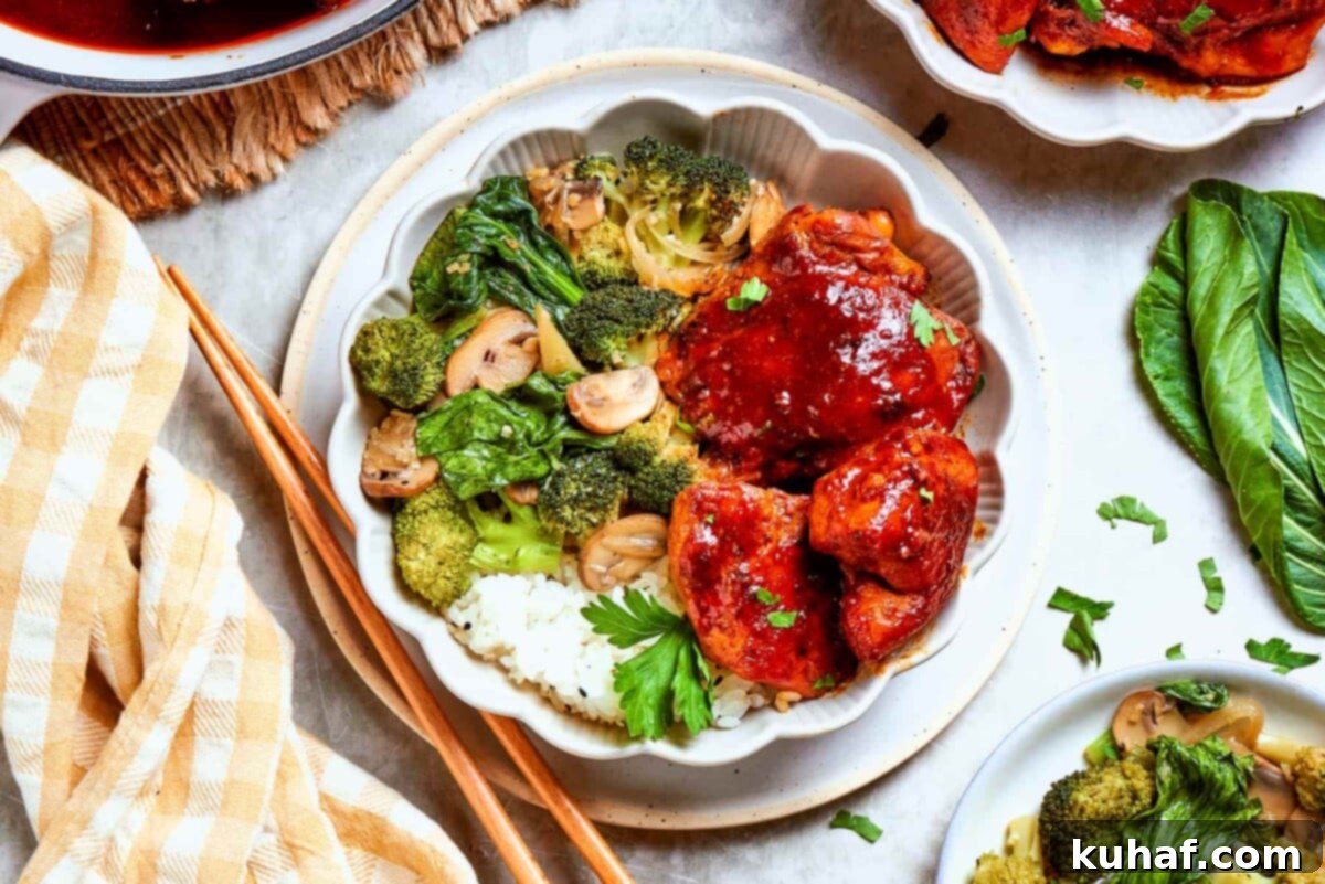 Gochujang chicken served with vegetables and rice on a white table with natural light, garnished with fresh herbs.