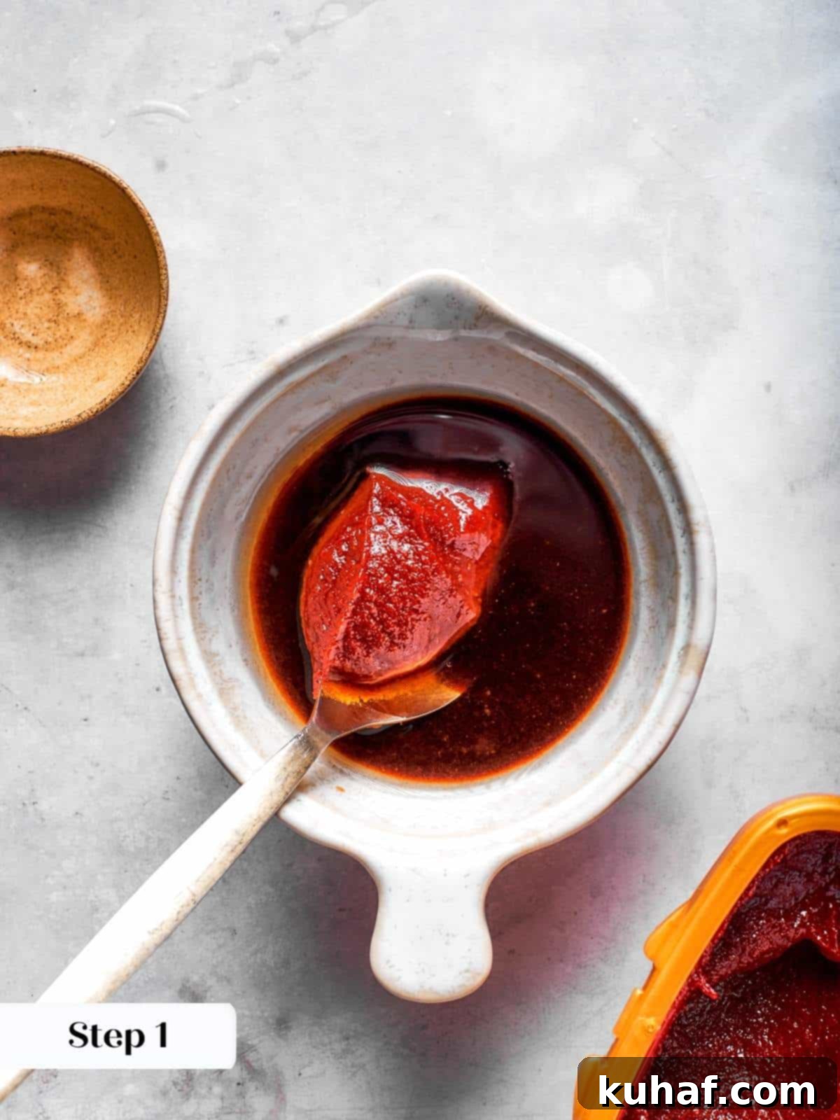 Combining ingredients for gochujang sauce in a bowl with a whisk before adding to the skillet, showing vibrant red paste.