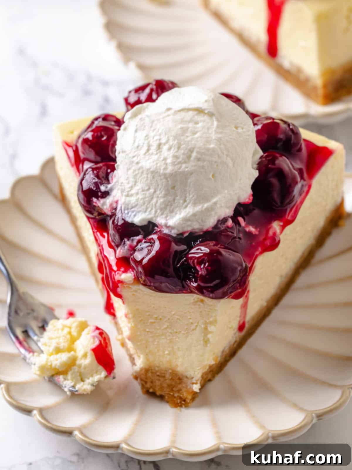 A slice of cheesecake with one bite taken, showing layers of crust, cream, and topping.