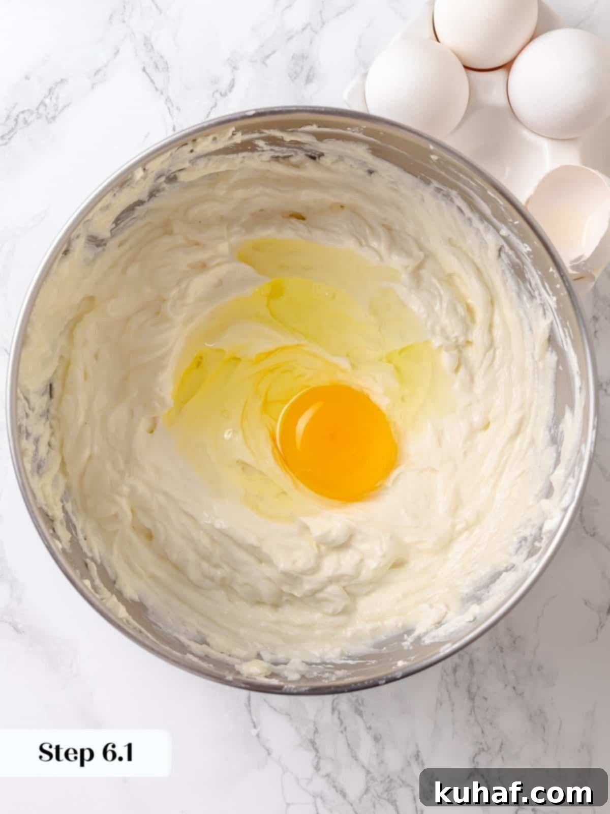 One egg being cracked into the batter as part of the cheesecake custard step.