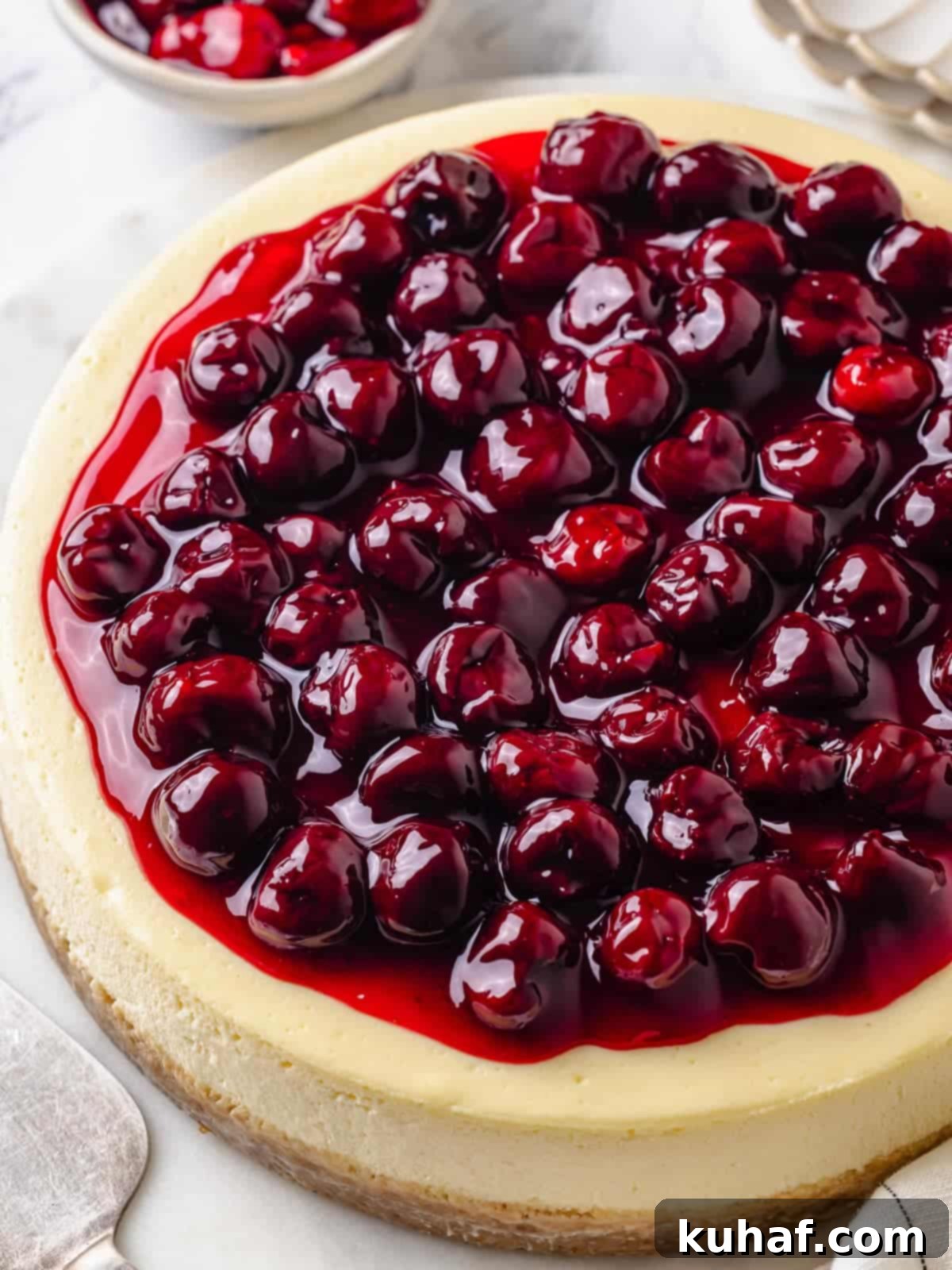 A whole cherry cheesecake with smooth filling and cherry topping on a white cake stand.
