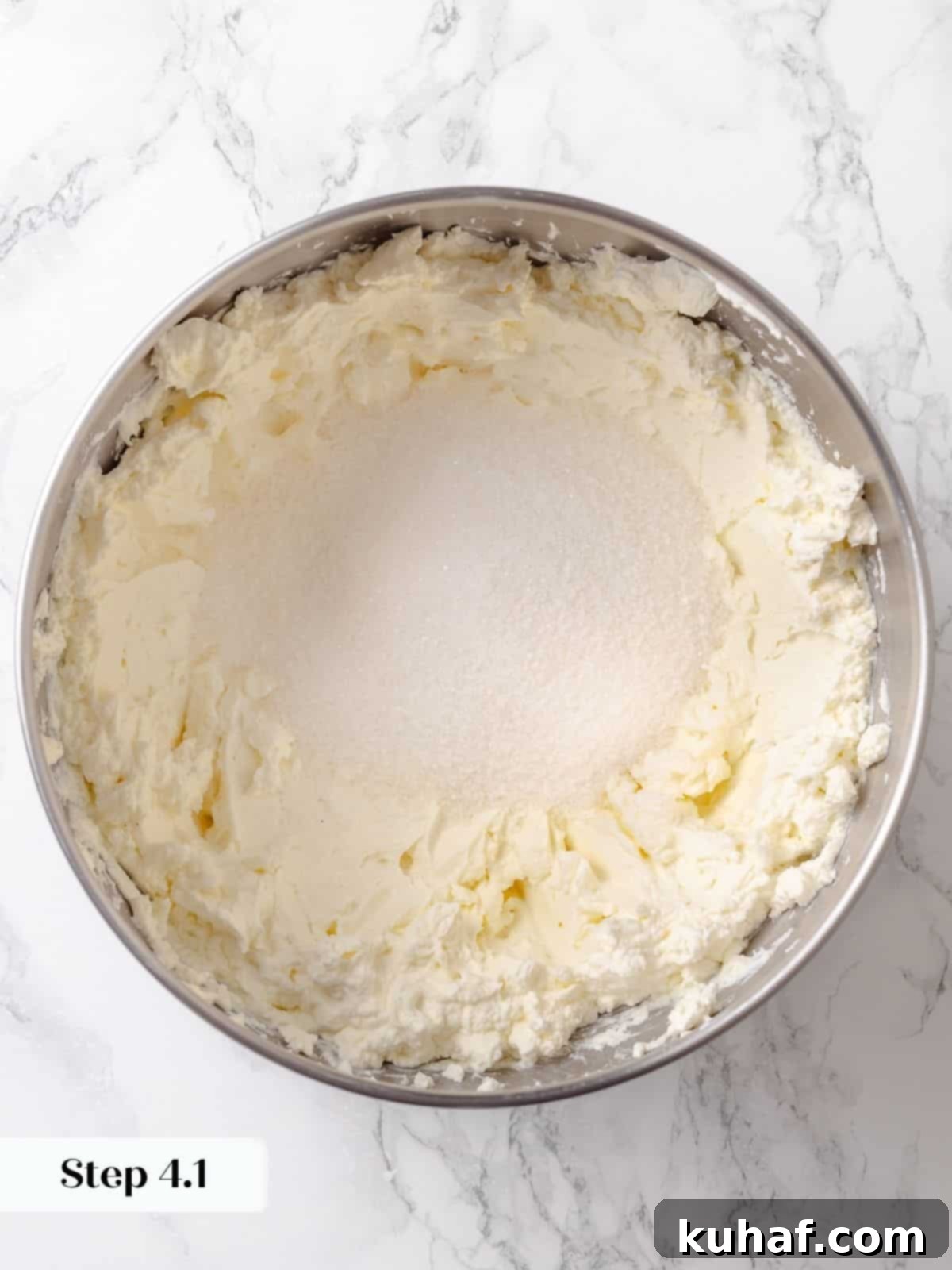 Sugar being added to the bowl of cream cheese during the cheesecake mixing process.