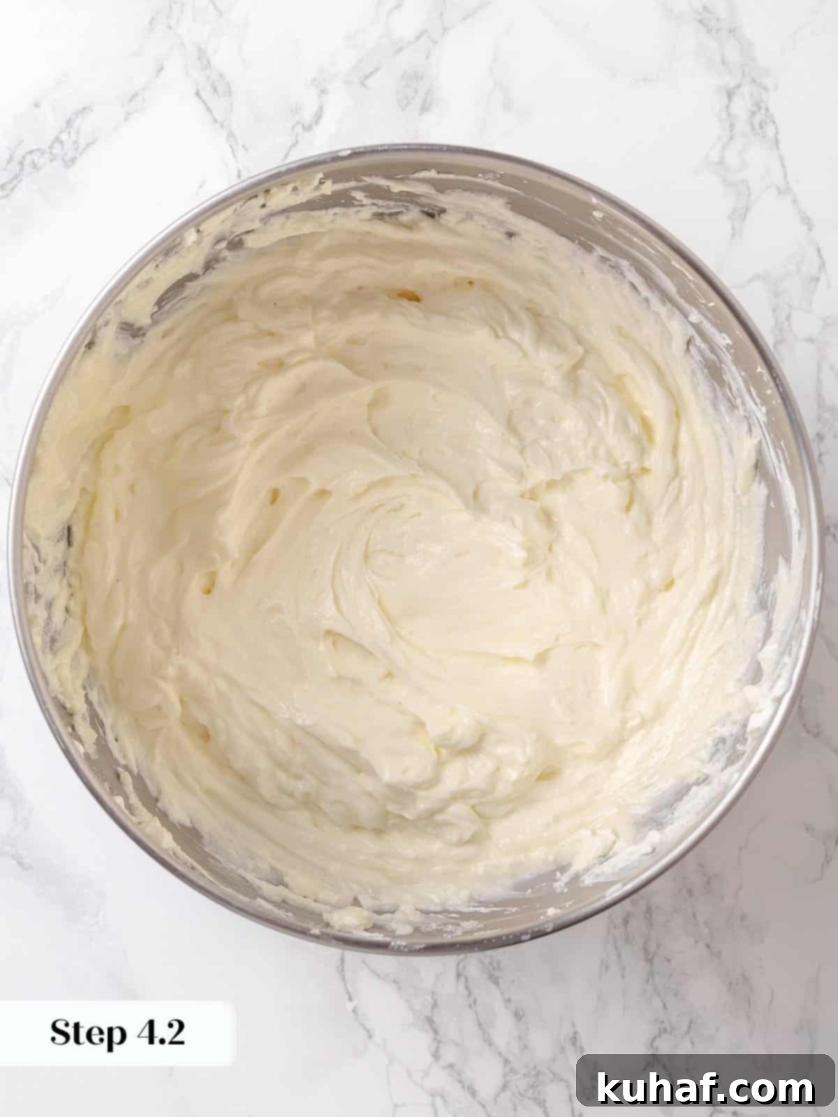 Granulated sugar being mixed into softened cream cheese for a silky cheesecake batter base.