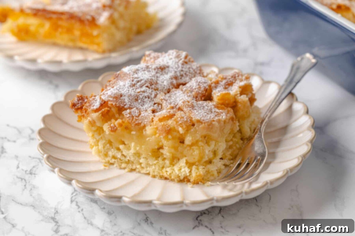 A fork by a piece of gooey butter cake showing layers of golden crust and filling.