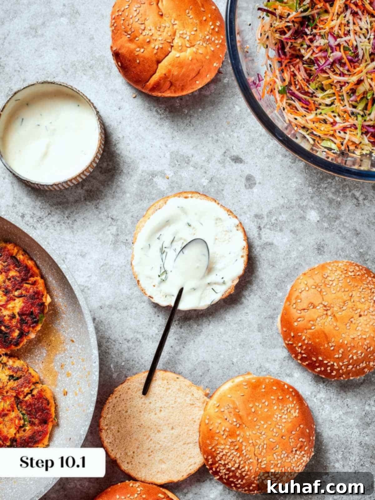 Bottom burger bun being spread with tzatziki as base for assembling a salmon burger.
