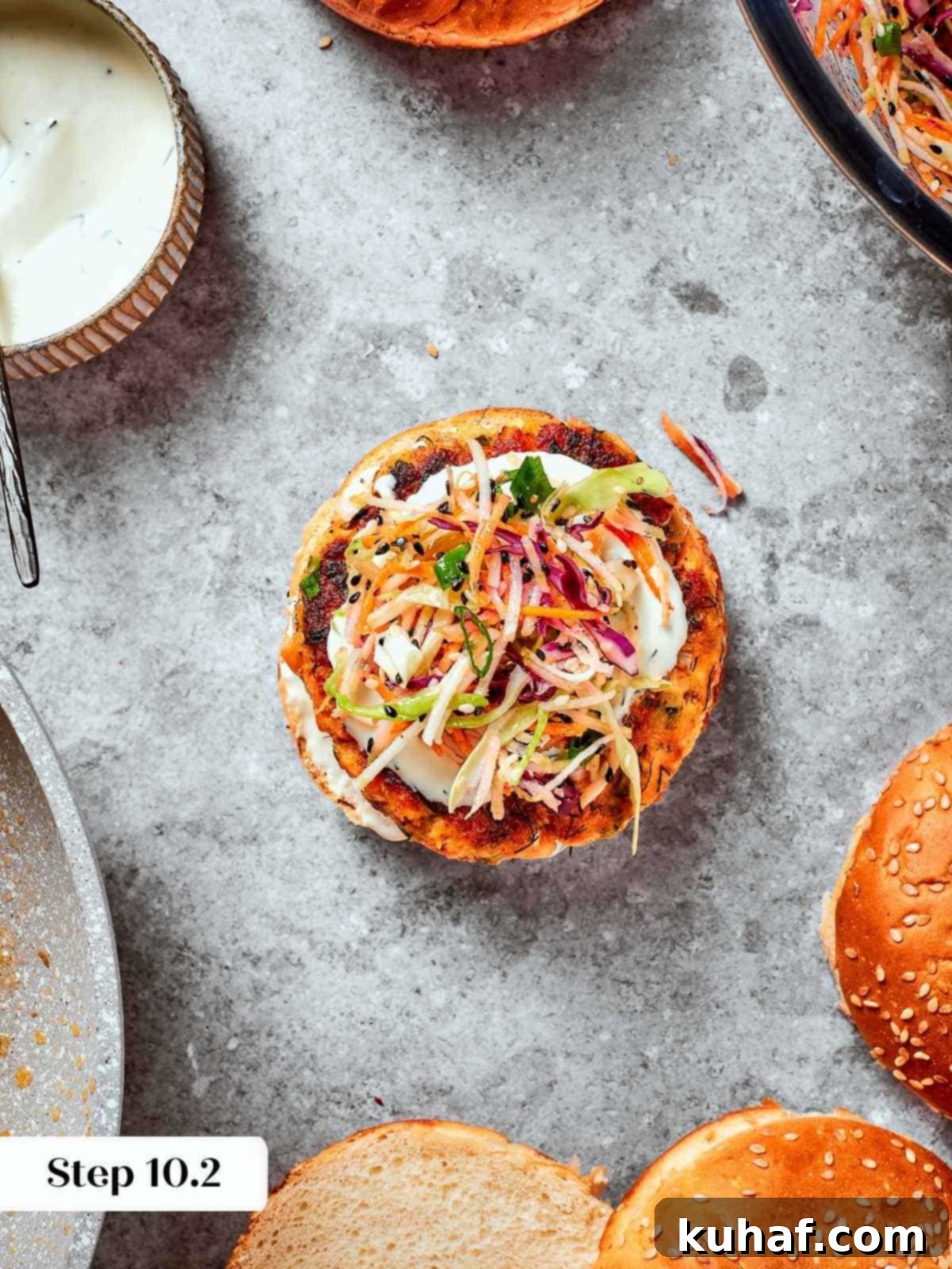 Assembled burger with top bun off showing layers of salmon, slaw, and sauce.