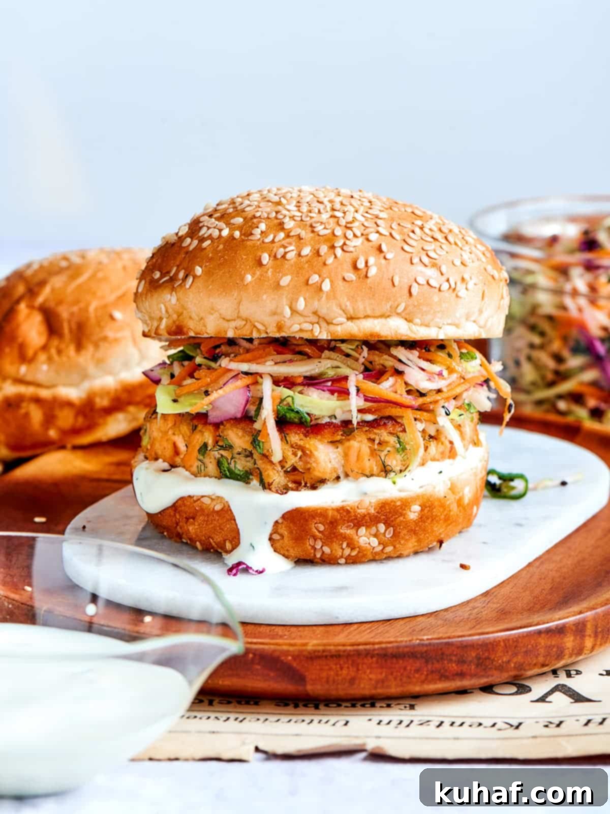 Salmon burger topped with sesame bun, served on wood with slaw spilling out.