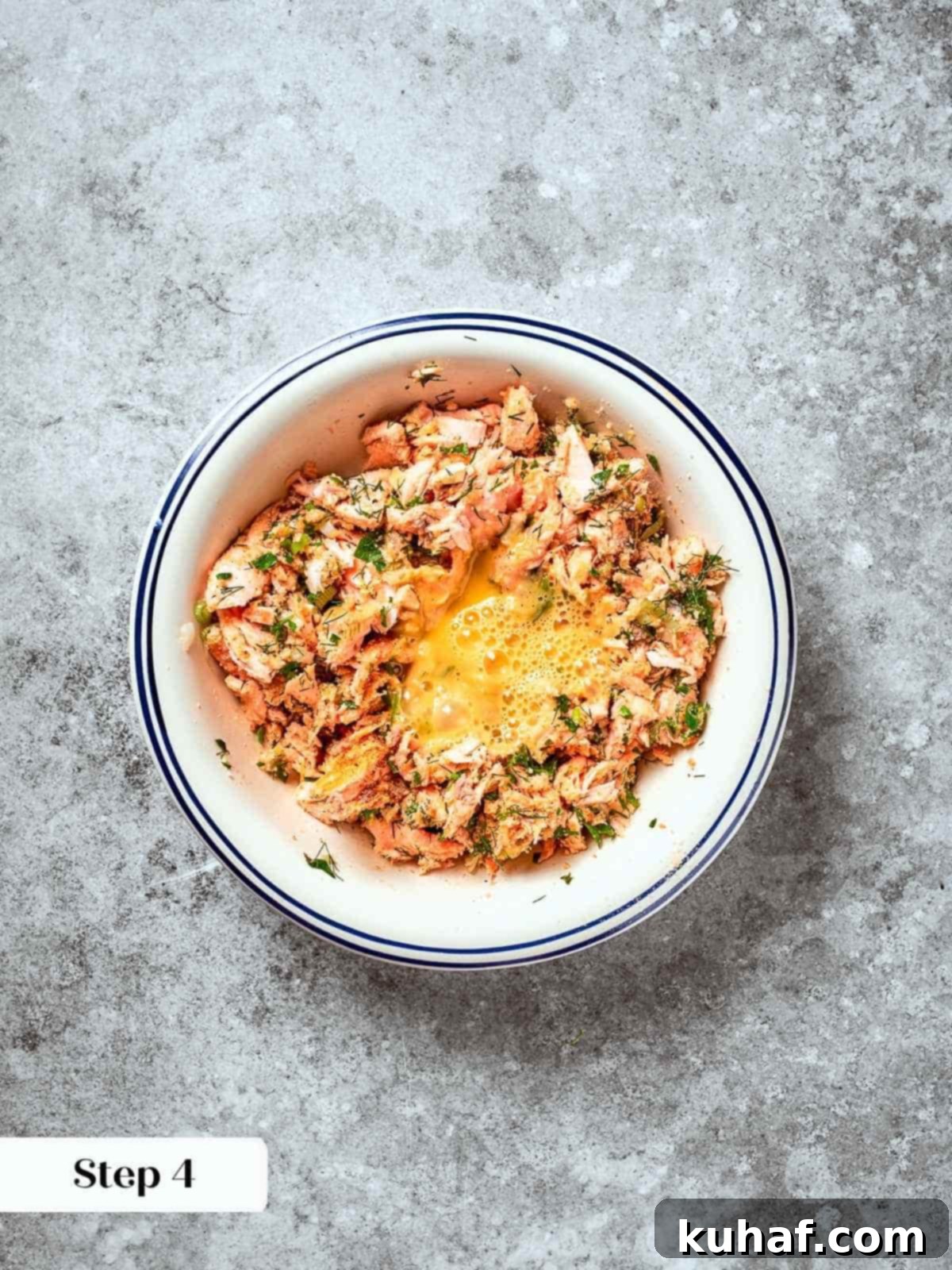 Egg being added to salmon patty mixture in a mixing bowl with herbs and breadcrumbs.