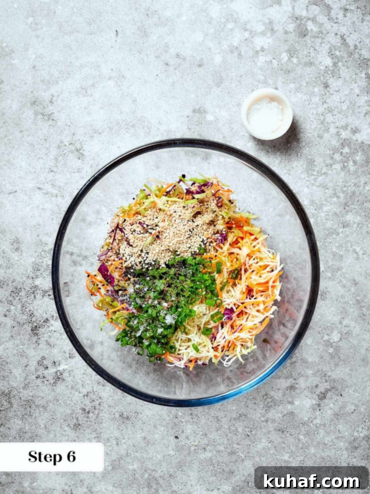 Mixing bowl filled with raw slaw ingredients, including broccoli mix and sesame seeds.