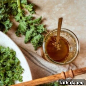 Jar of homemade Italian salad dressing set beside fresh kale leaves on a kitchen counter.