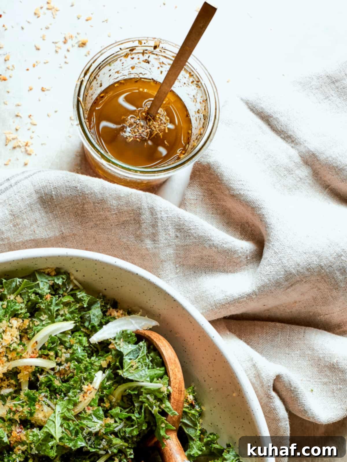 Clear glass jar of homemade Italian salad dressing resting on a white counter near a soft cloth napkin.