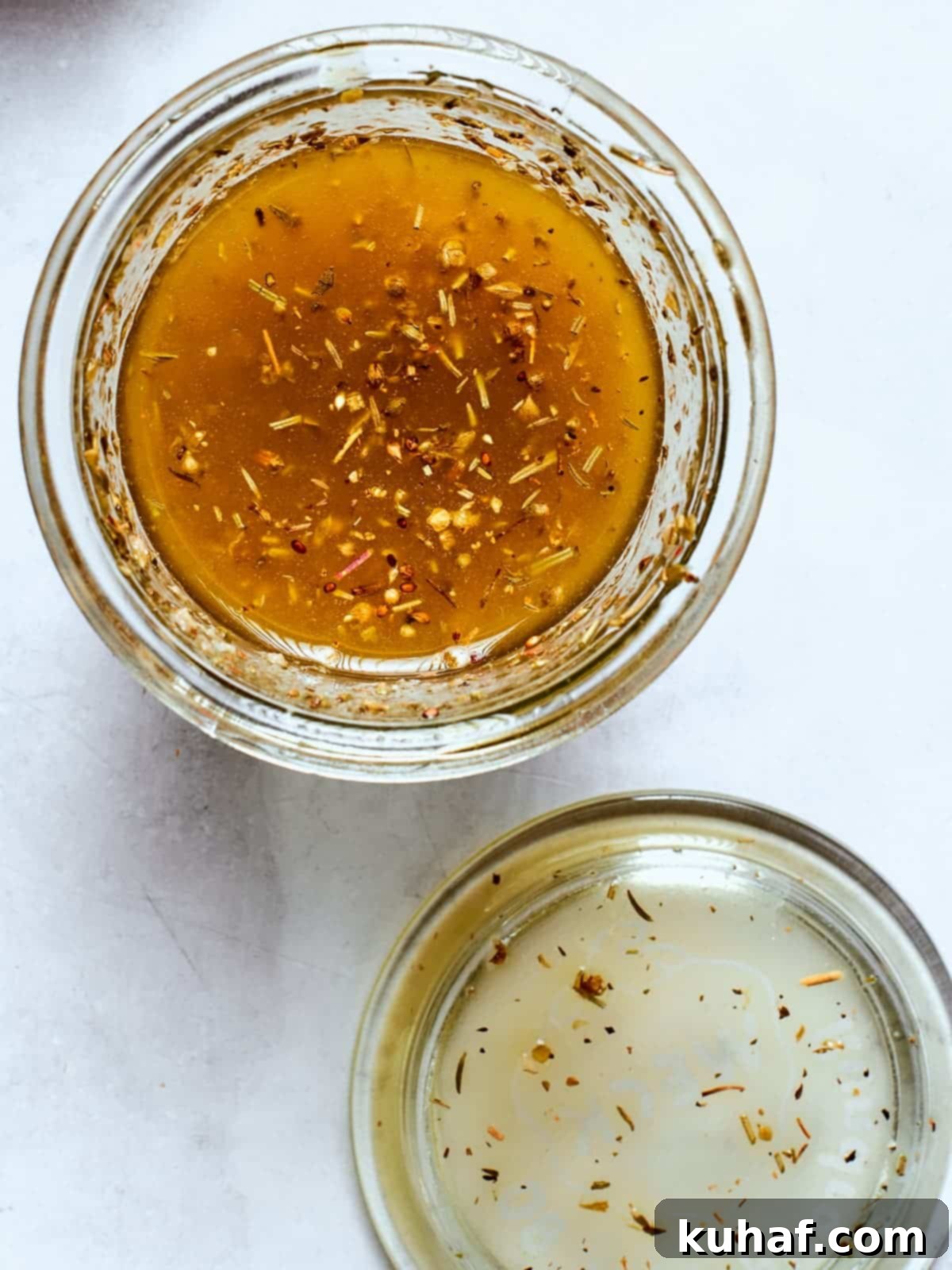 Clear glass jar filled with Italian salad dressing, showcasing visible herbs and spices suspended in the liquid.