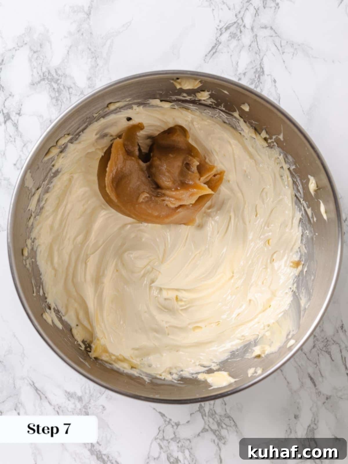 Golden Maple Frosting 10 The cooled maple mixture is being added spoonful by spoonful to the whipped butter in a stand mixer bowl, gradually creating a smooth frosting.