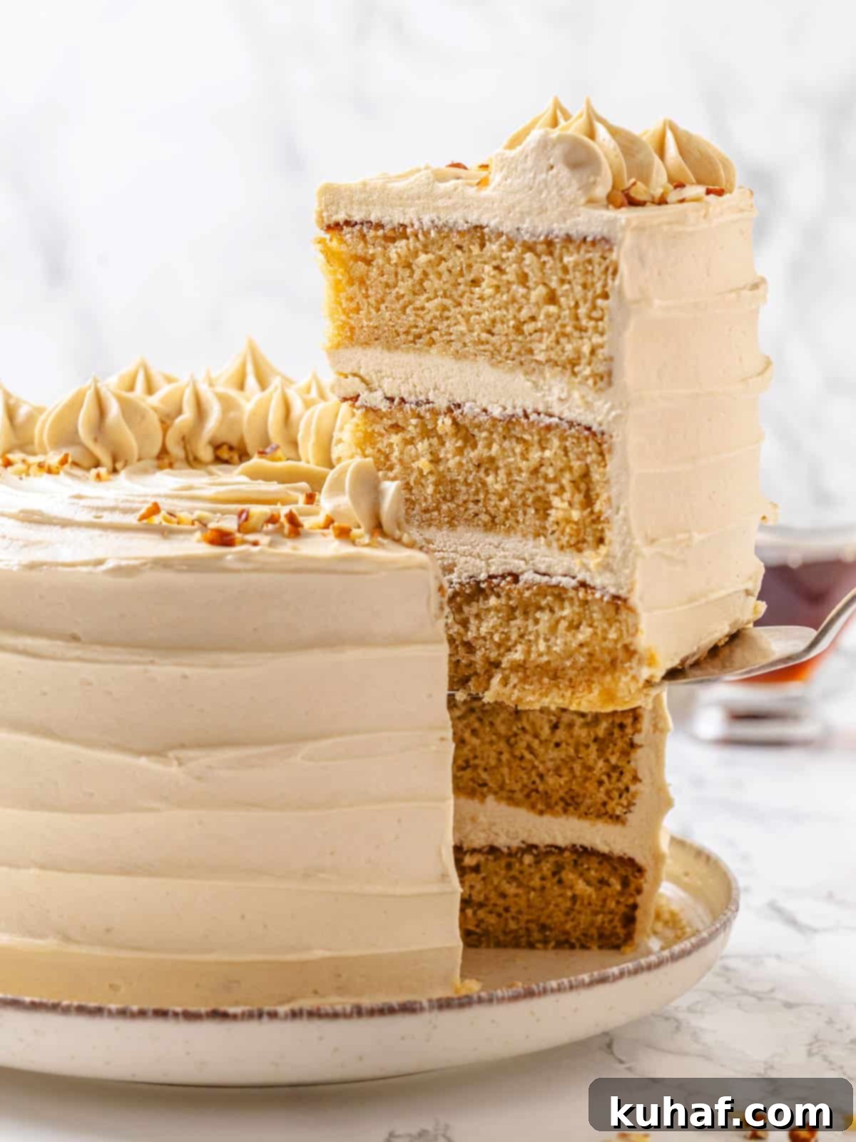 Pure Maple Indulgence 19 A beautiful slice of maple cake being lifted from the whole cake with a serving utensil, showing off its soft layers and fluffy frosting.