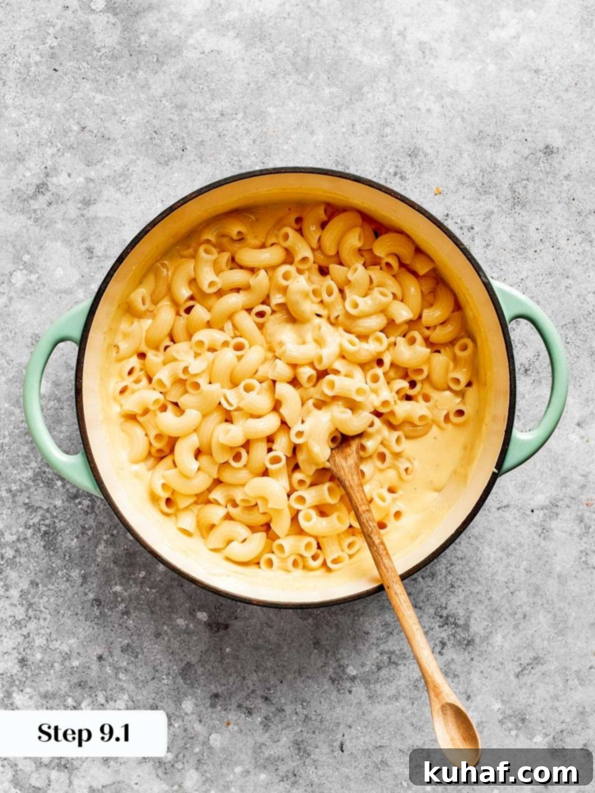 Cooked pasta being gently folded into a luscious, creamy cheese sauce in a large mixing bowl.