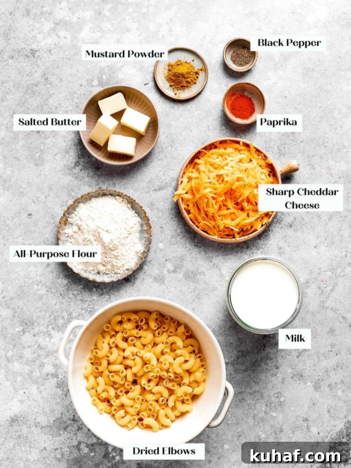All the fresh ingredients for homemade baked mac and cheese, including pasta, cheese, milk, butter, and spices, spread out on a clean countertop.
