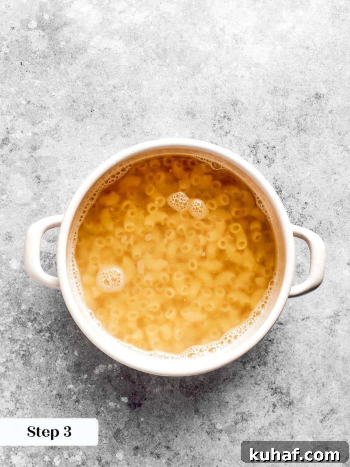 A large pot of water boiling vigorously on a stovetop with elbow macaroni cooking inside.