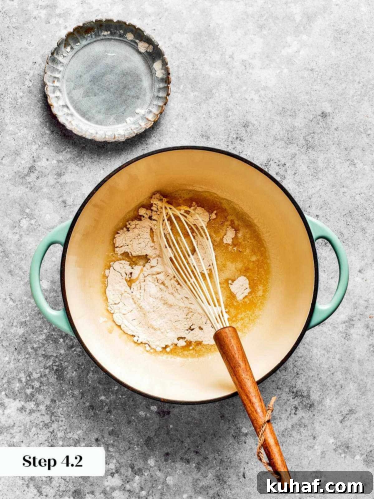 All-purpose flour being meticulously stirred into melted butter in a saucepan to begin the roux for the mac and cheese sauce.