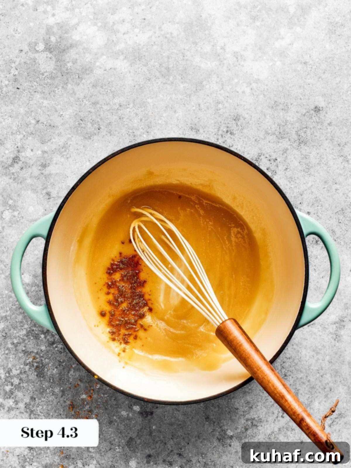A whisk stirring ingredients in a saucepan over low heat, showing the beginning of the roux formation.