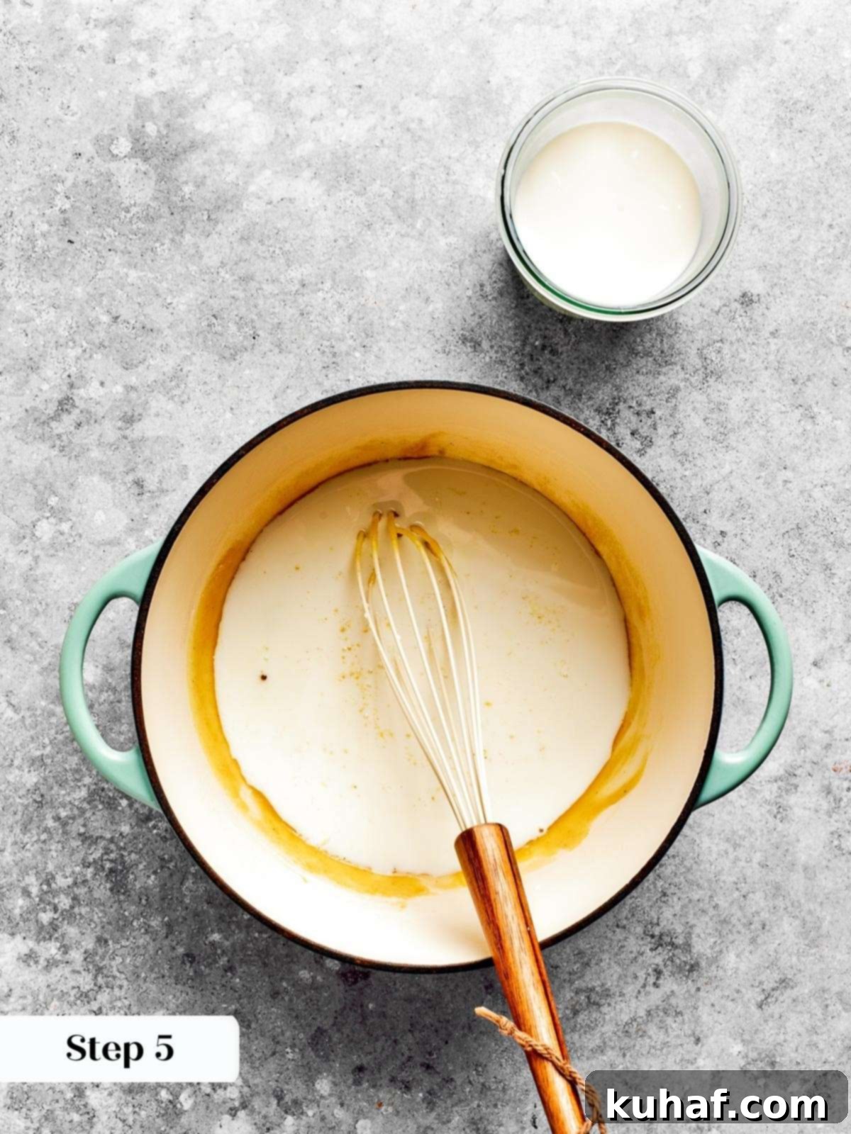 Fresh, cold milk being slowly poured into a warm, thickened roux while being continuously whisked for a smooth sauce.