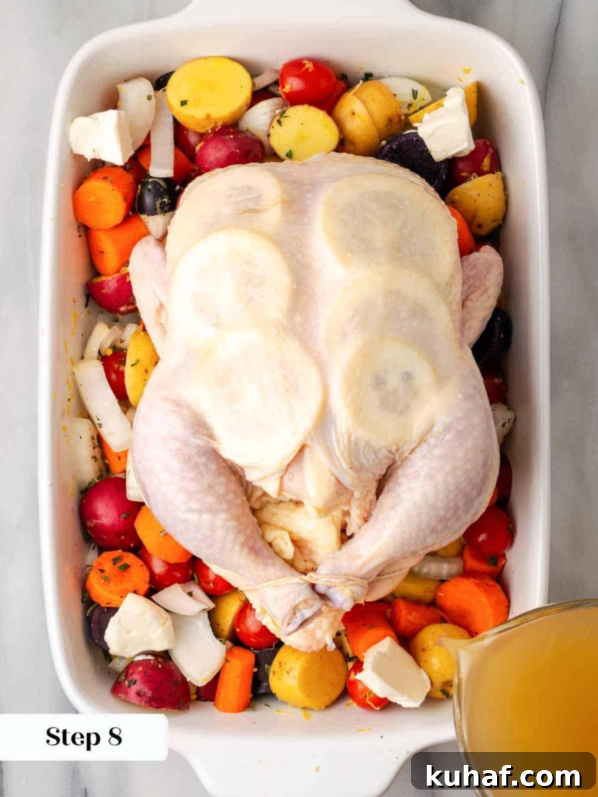 trussed chicken on vegetables in white roasting dish.
