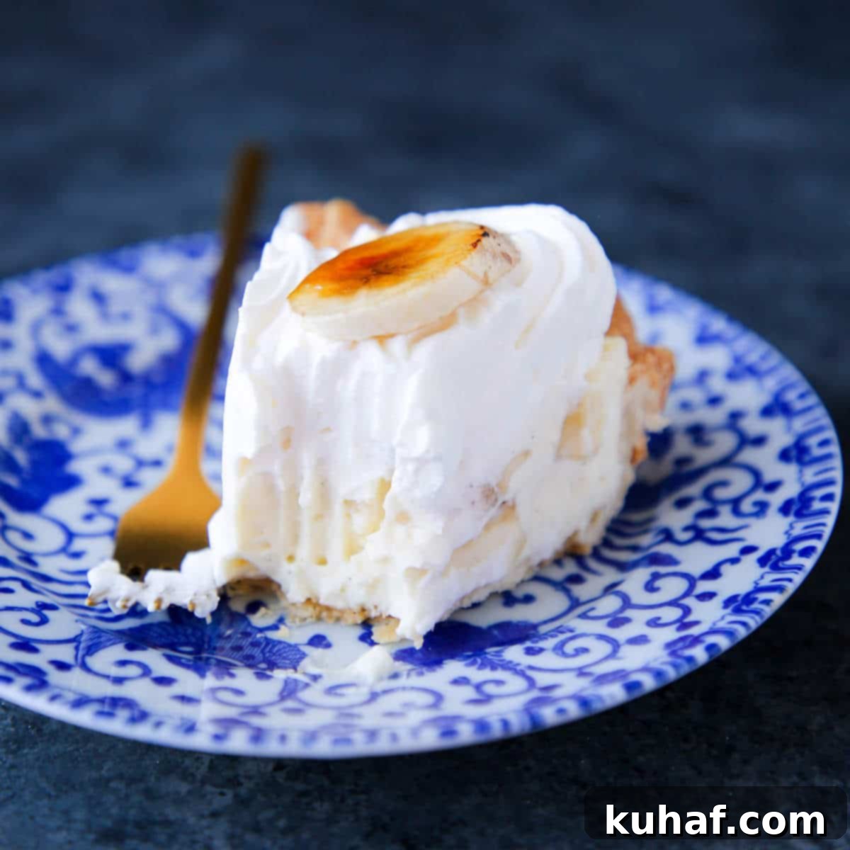 A slice of creamy Banana Cream Pie, layered with golden pastry cream and fluffy whipped cream, served on a blue plate.