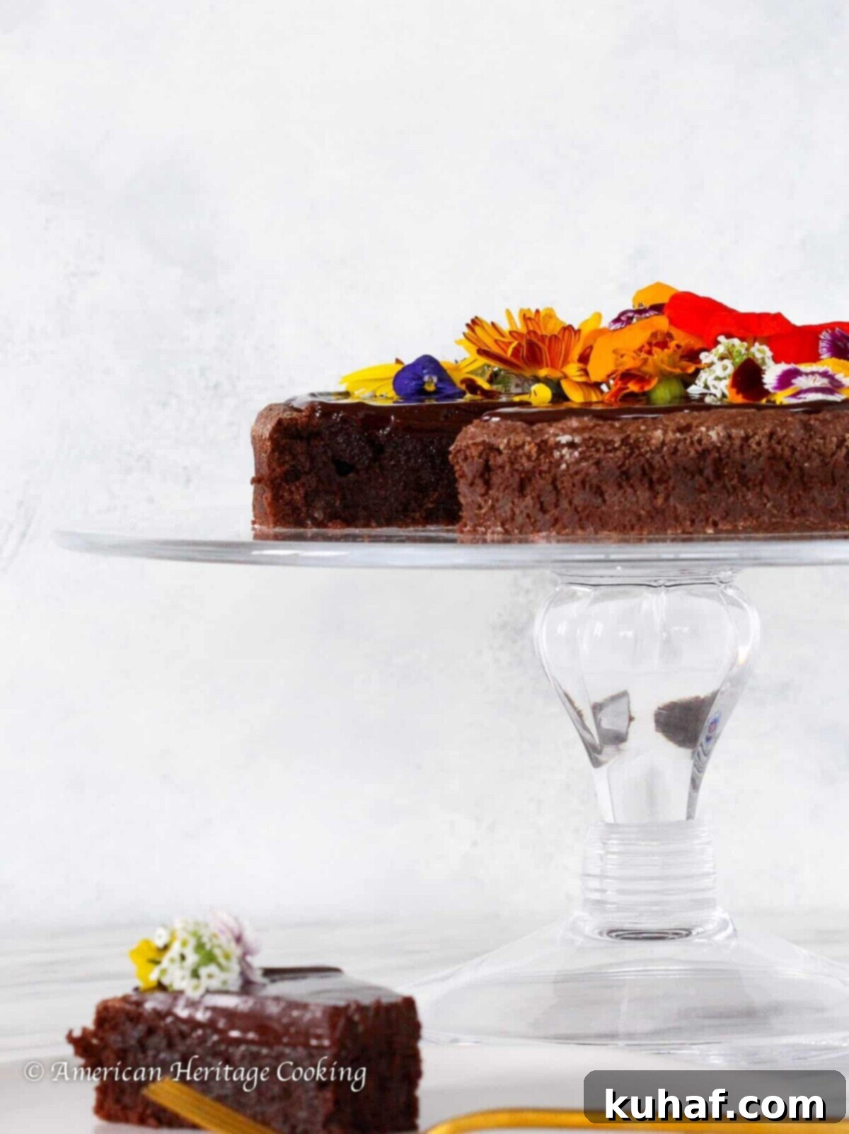 Flourless Chocolate Torte on a clear cake stand, garnished with edible flowers, perfect for Valentine's Day Desserts or any special occasion.