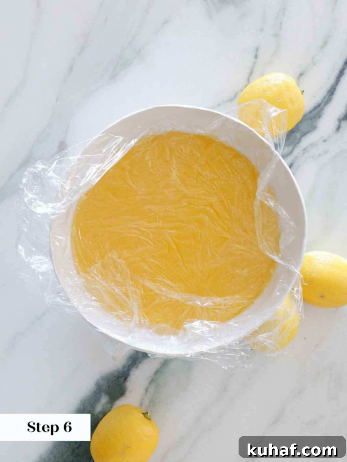 cooling lemon curd with plastic wrap on surface in white bowl.