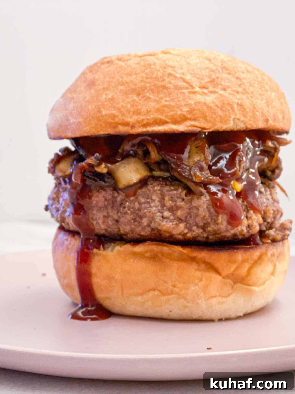 tall burger on bun on pink plate.