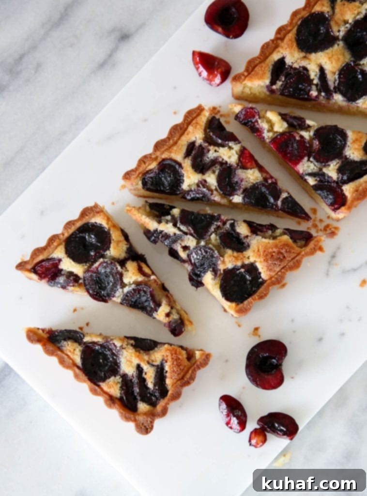 A delicious Cherry Almond Tart with a crispy almond sablée crust, soft almond cream filling, and jammy baked fresh cherries, served on a marble board.