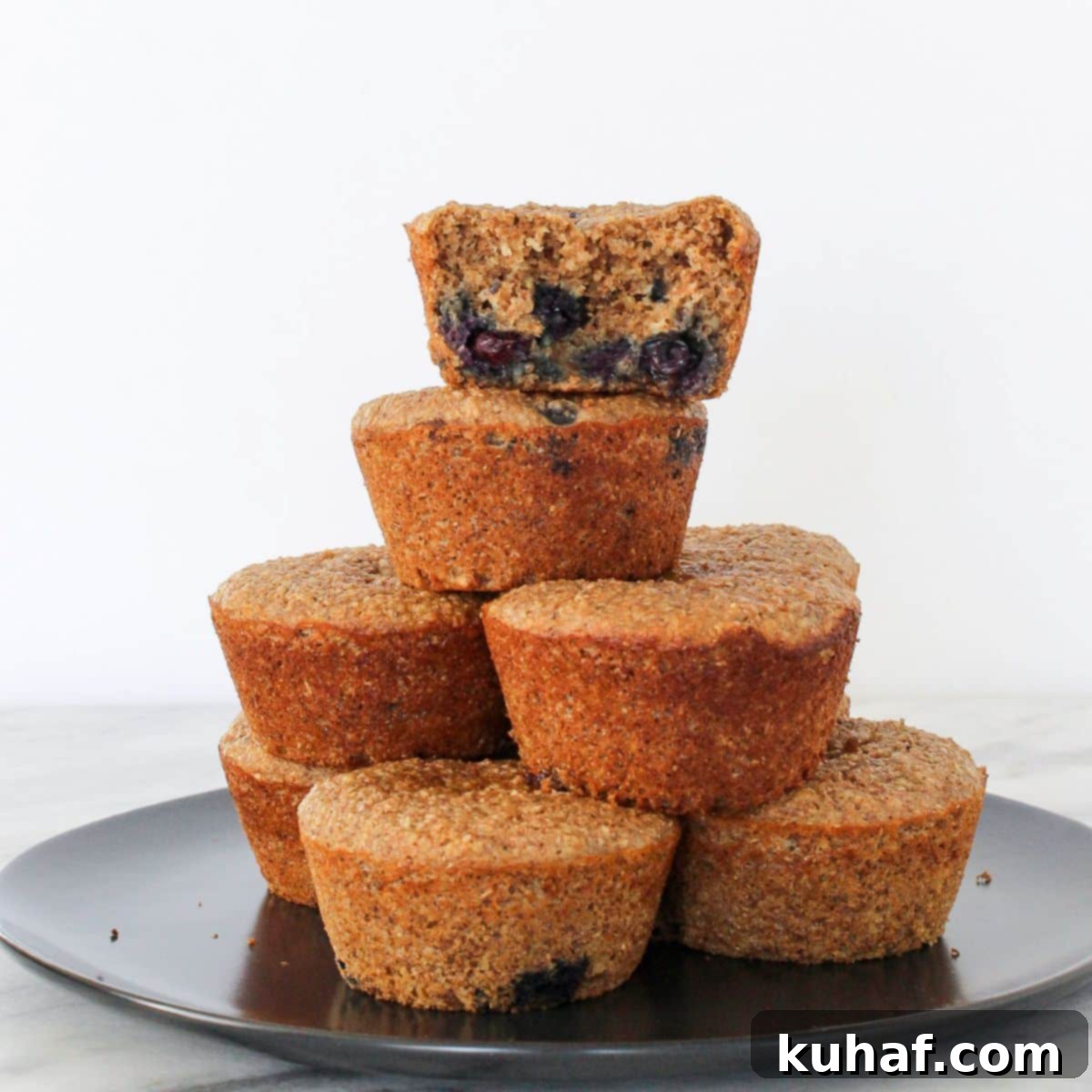 A banana protein muffin with one bite taken, stacked with others to show soft inside texture.