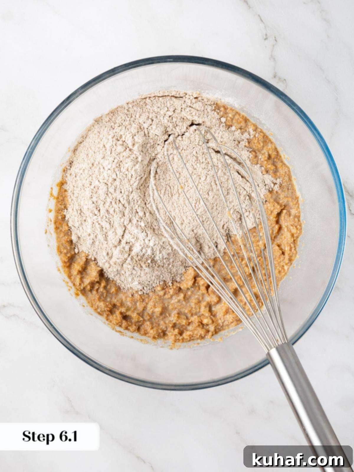 Flour mixture being added to a bowl of wet ingredients while making banana protein muffin batter.