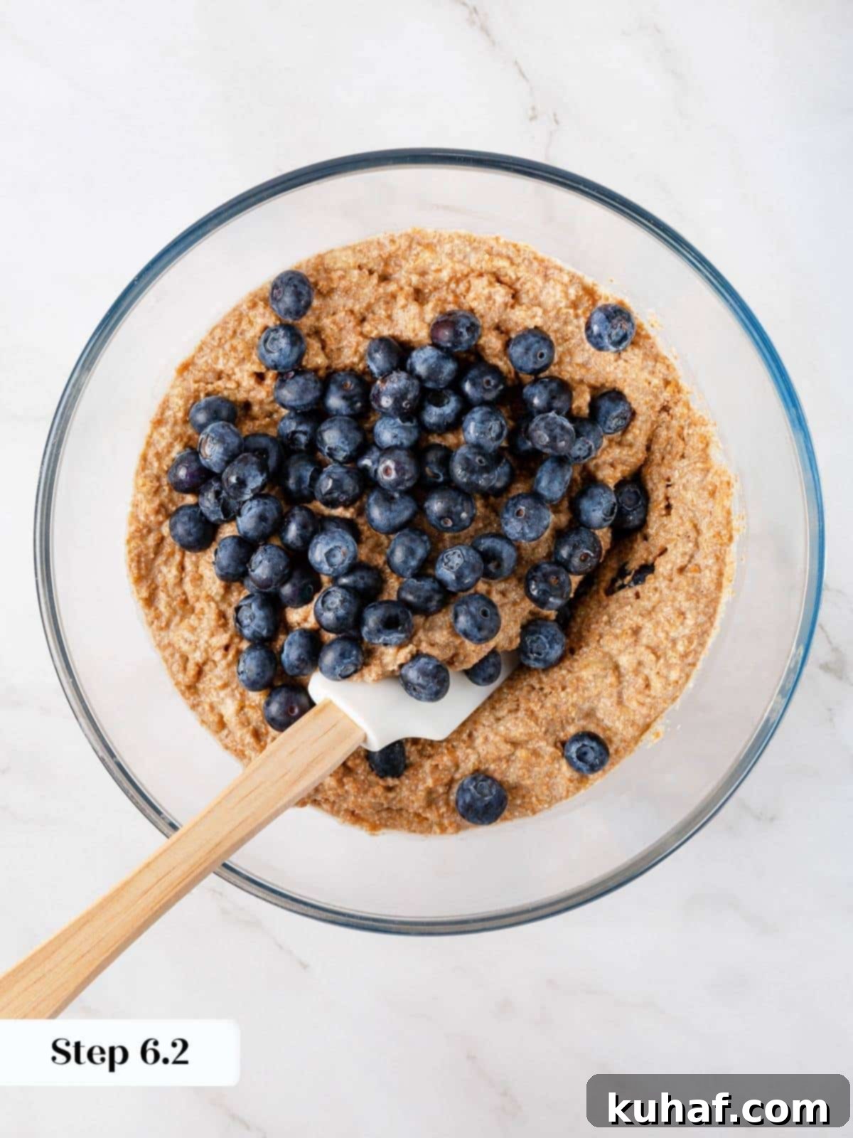 Blueberries gently folded into banana muffin batter with a spatula to avoid overmixing.
