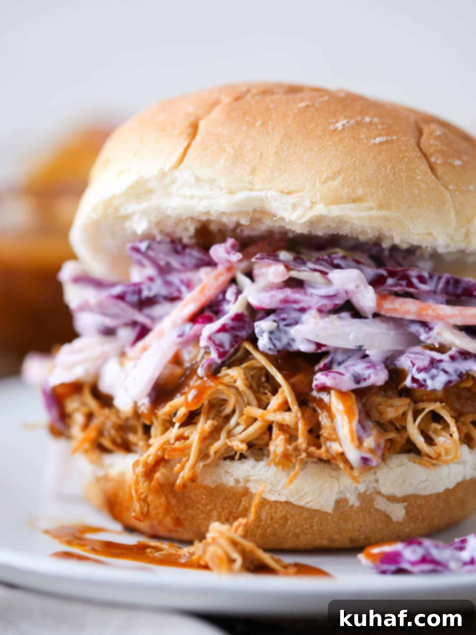 A close-up shot of a slow cooker barbecue pulled chicken sandwich on a wooden board, garnished with fresh herbs, showcasing the succulent chicken and coleslaw.