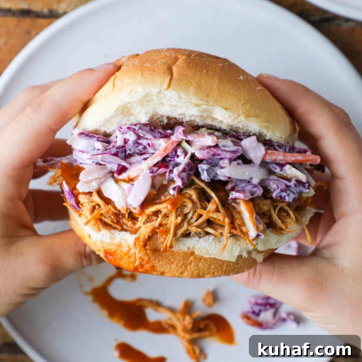 A hand holding a slow cooker barbecue pulled chicken sandwich, showing the generous filling of chicken and coleslaw, ready to be enjoyed.