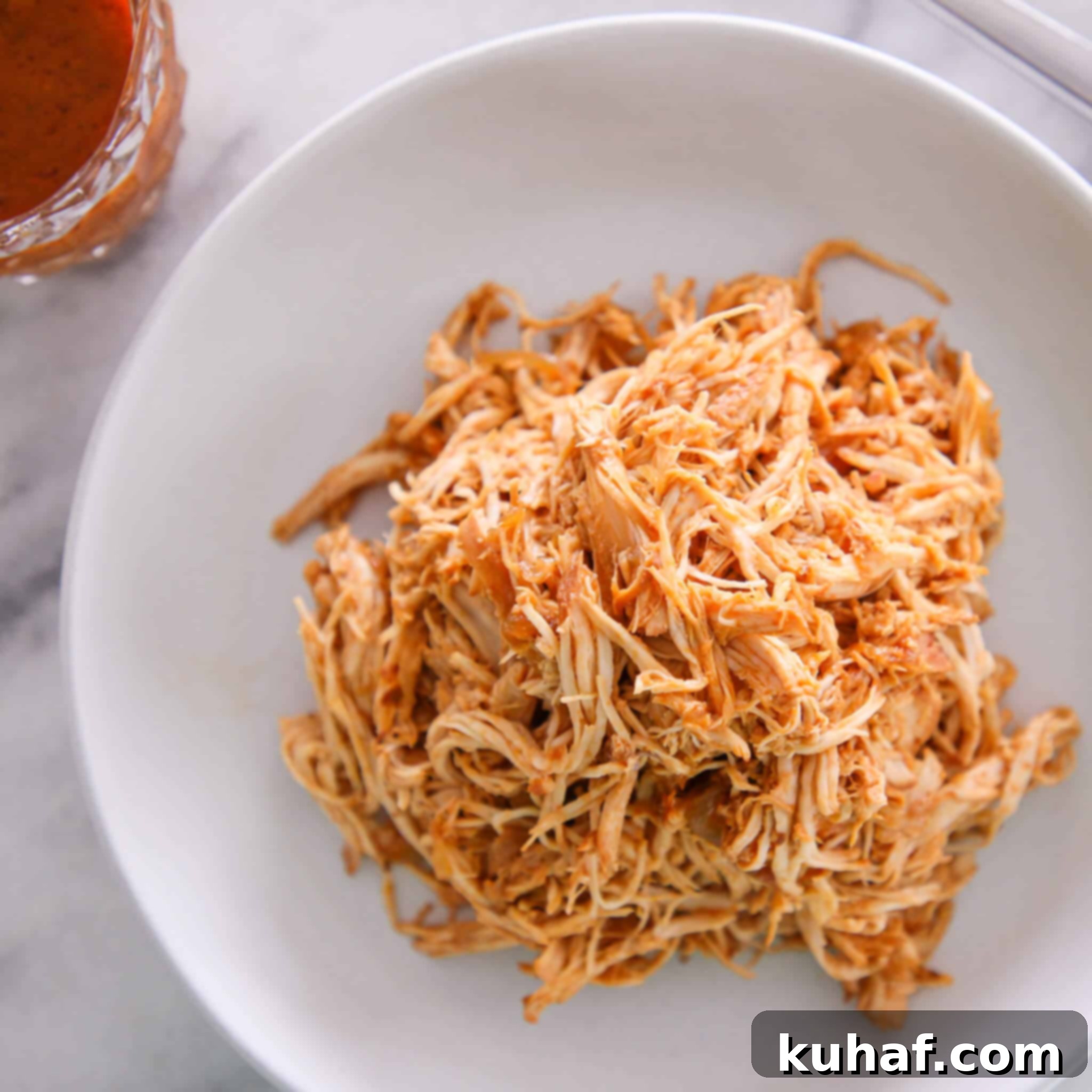 A white bowl filled with slow cooker barbecue pulled chicken, showing the rich, saucy texture of the shredded meat.