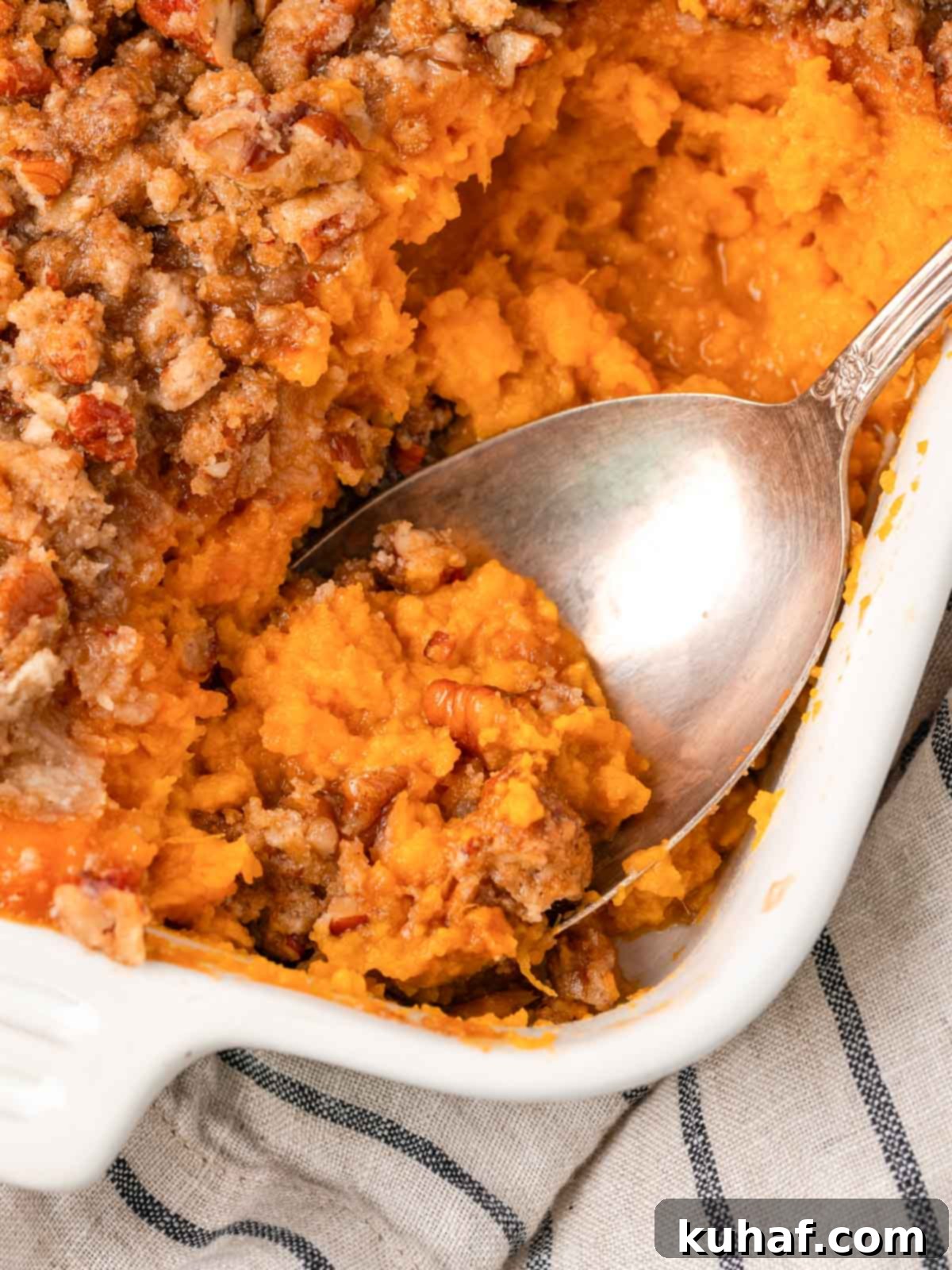 Decadent Sweet Potato Casserole with Crunchy Pecans 2 Creamy sweet potato casserole in a white baking dish with a serving spoon, ready to be enjoyed.