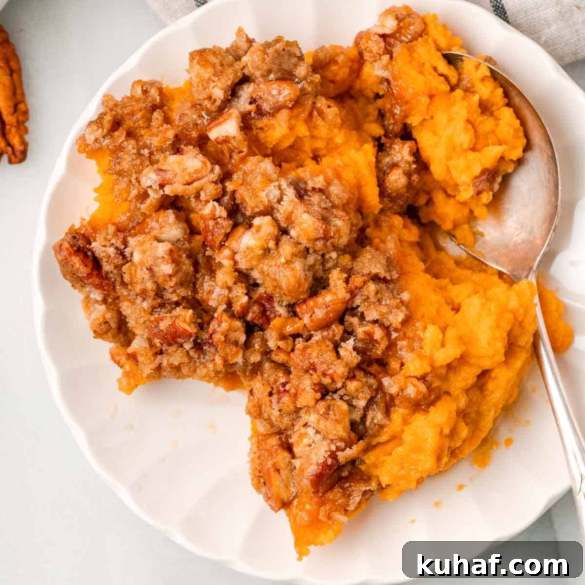 Decadent Sweet Potato Casserole with Crunchy Pecans 11 A serving of sweet potato casserole with the pecan topping on a white plate, ready to be eaten.