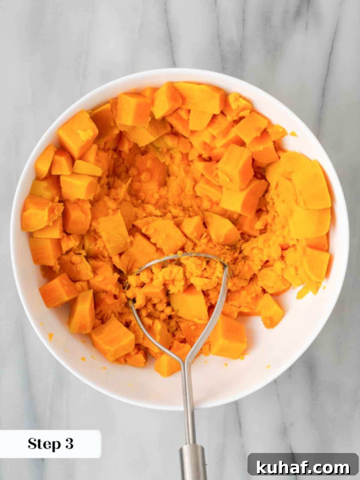 Decadent Sweet Potato Casserole with Crunchy Pecans 6 Mashing sweet potatoes in a bowl with a potato masher, creating a smooth puree.