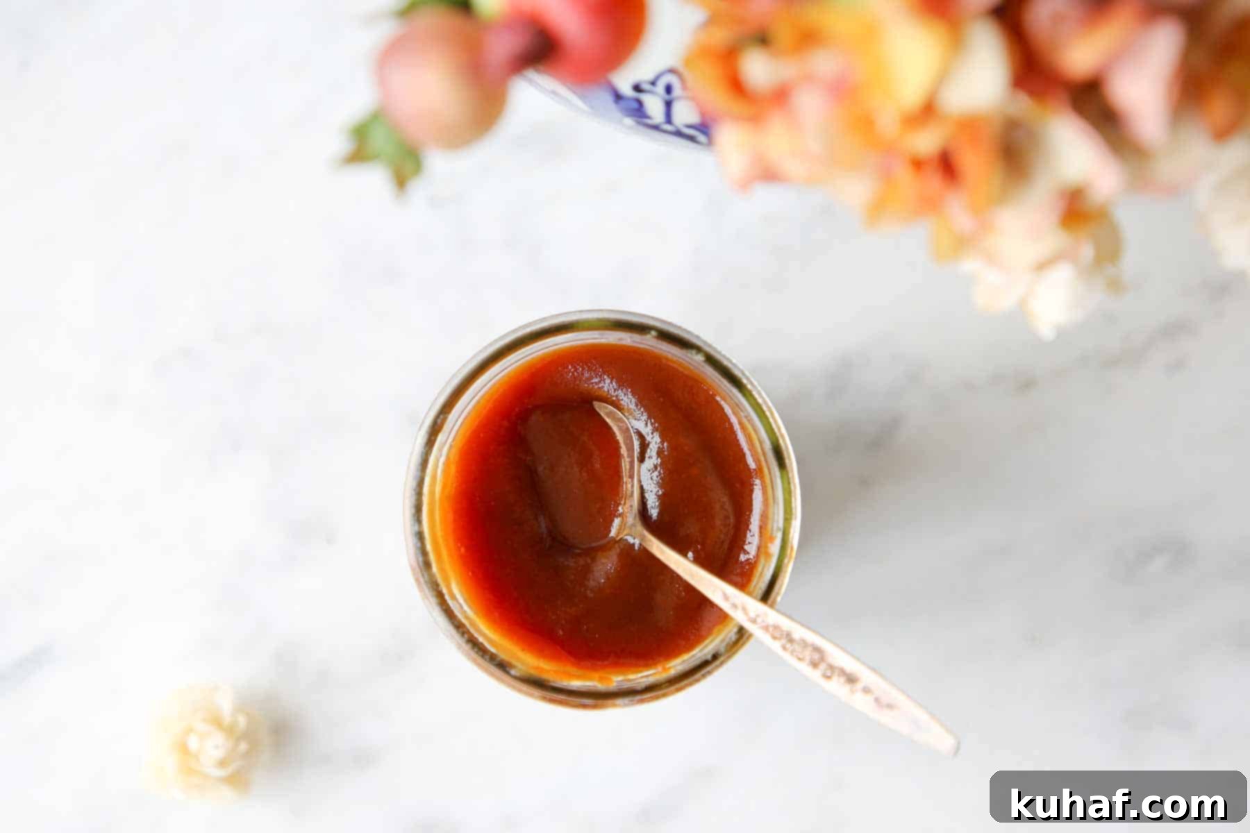 Caramelized Apple Spread 3 Homemade apple butter on marble with decorative fall flowers, showcasing its beautiful texture.