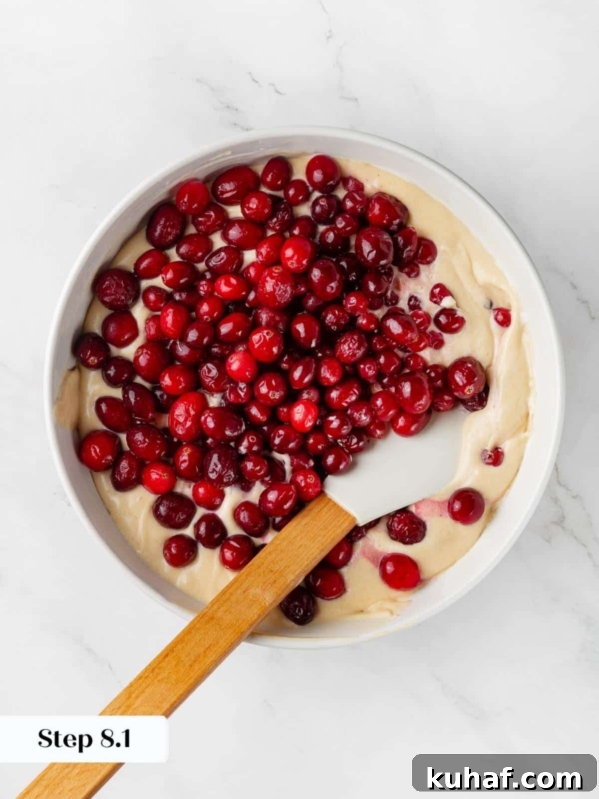 Fresh cranberries being folded into light cake batter with a spatula.
