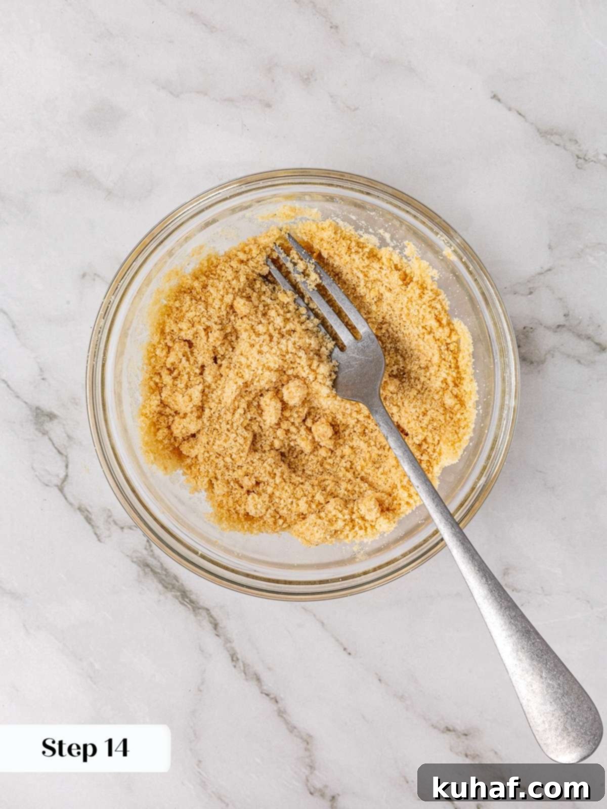 Brown sugar crumble mixture forming in a clear glass bowl after being stirred with melted butter and vanilla, showing a coarse, sandy texture.