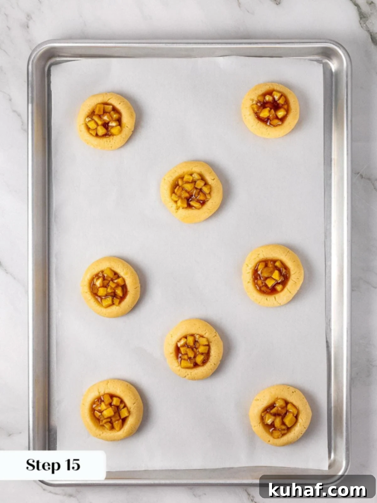 Unbaked cookie dough rounds on a baking tray, each generously filled with small spoonfuls of the prepared homemade apple pie filling.